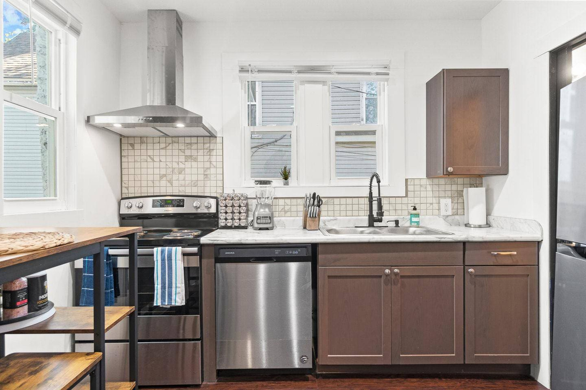 Enjoy cooking in this spacious kitchen, featuring rich brown cabinetry, a full set of modern appliances including an oven, stove, and dishwasher, plus bright windows that let in plenty of natural light. 