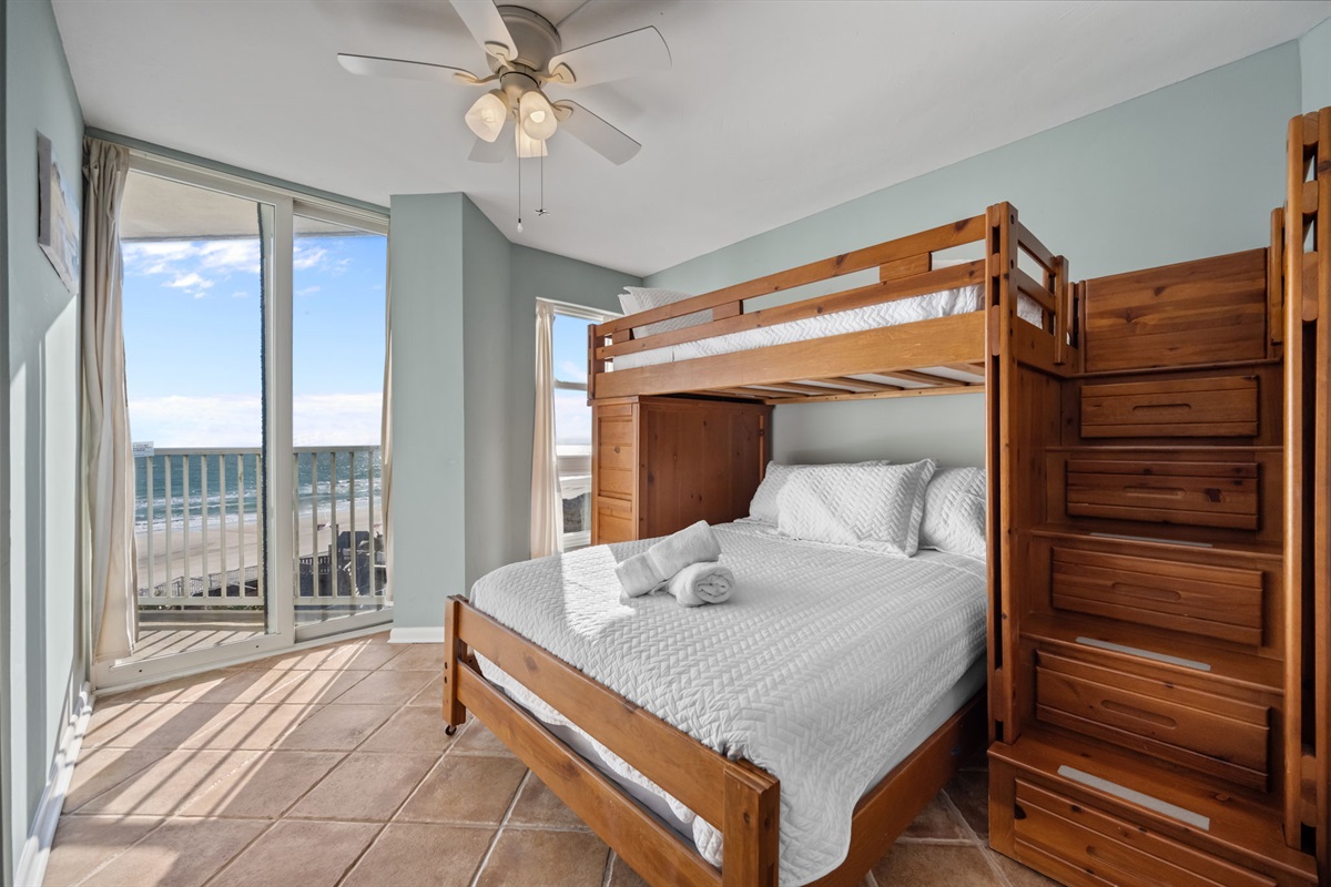 Bright bunk room featuring ocean views, a ceiling fan, and sliding doors that fill the space with natural light