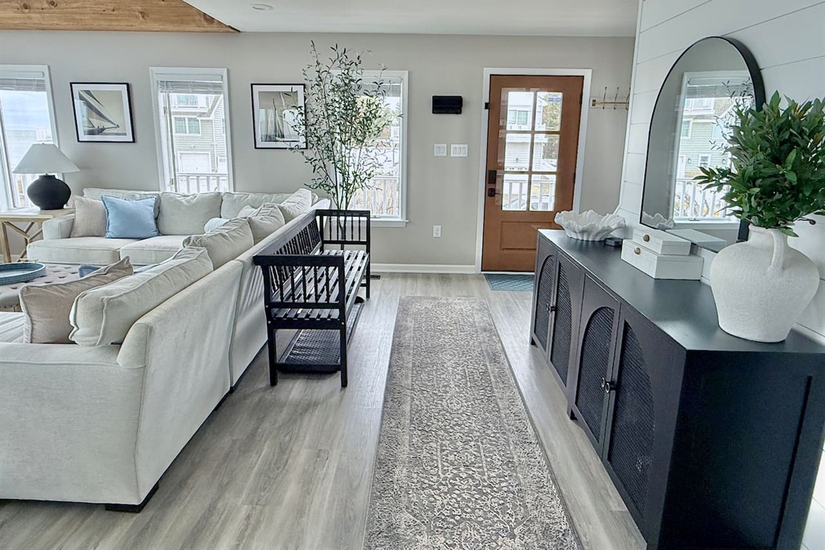 This living area bridges lounge and entry spaces with a large sectional, black accent bench, and cabinet with an arched mirror, perfectly enhancing the home's coastal aesthetic.