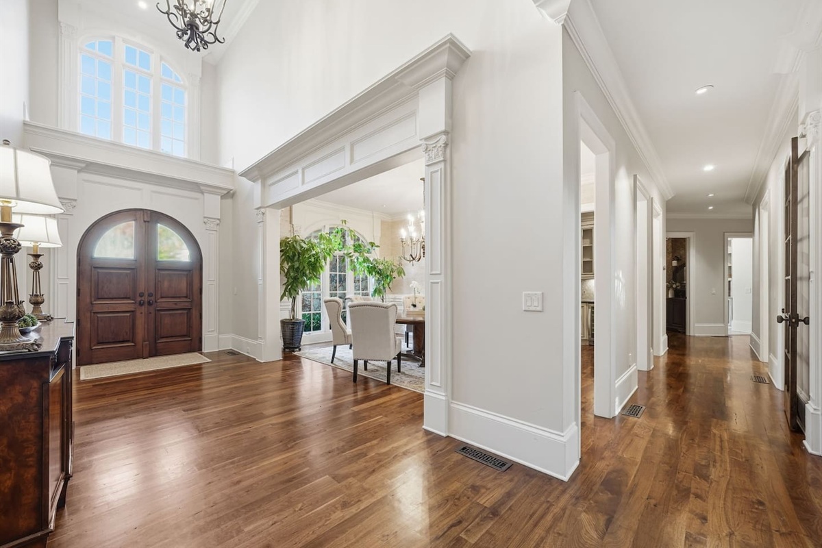 Spacious main dining room to the left of the foyer, featuring a chandelier, seating for seven, and lush green plants. A bright, welcoming space perfect for shared meals or special gatherings.