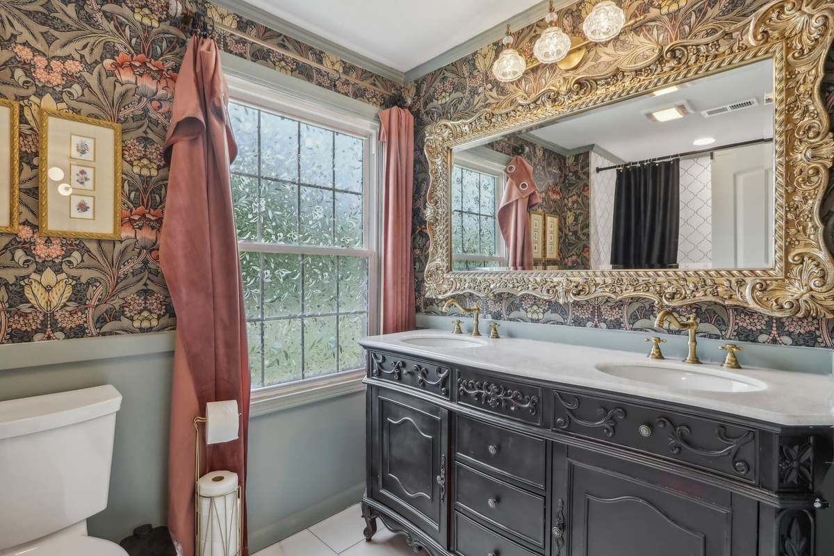 Elegant full bathroom, with a spacious double vanity, ornate mirror, and rich botanical details.