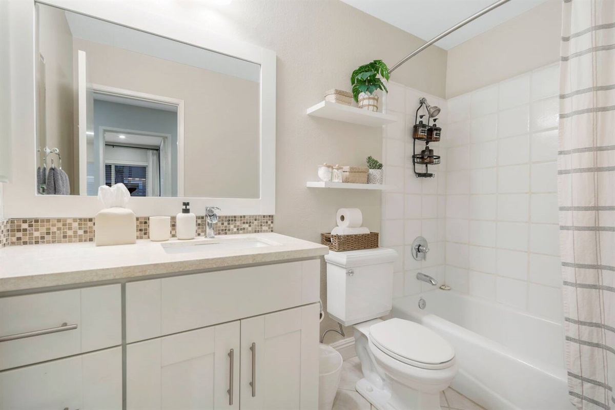 This bathroom is equipped with a tub and a shower, offering both relaxation and convenience. Shampoo, conditioner, and body wash &  plush towels are available for guests, providing a complete and comfortable experience.