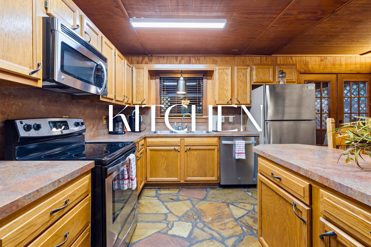 Rustic kitchen with stainless appliances and forest views.