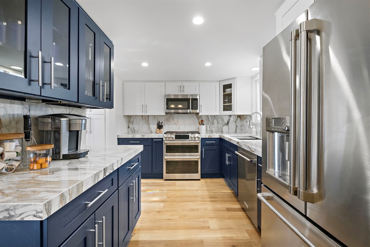 Another view of the chef-ready kitchen showcasing custom cabinetry, marble countertops and backsplash, and premium appliances — thoughtfully stocked with cookware, utensils, and serving pieces for everything from quick breakfasts to a full holiday meals.