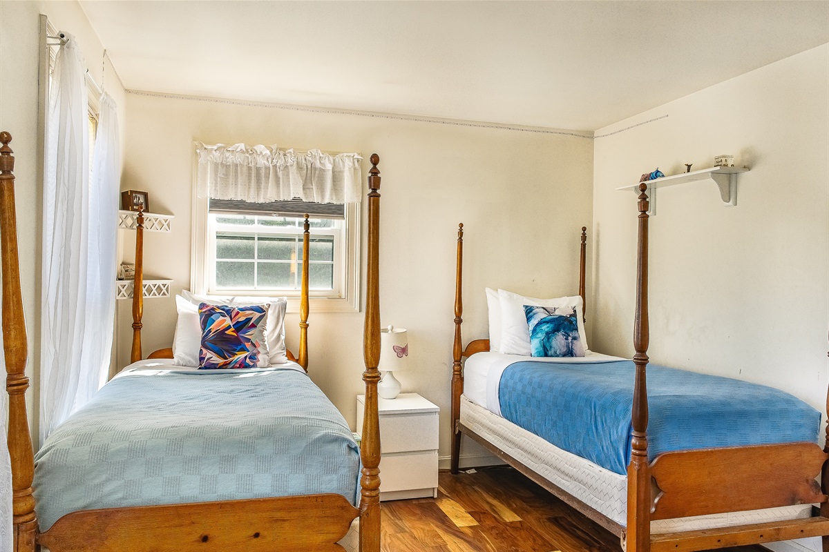 The dual twin guest room features charming antique four-poster beds and hardwood floors. Equipped with blackout blinds and dedicated summer AC, this bright space offers a cool, restful retreat for children or singles on the "Quiet Side."