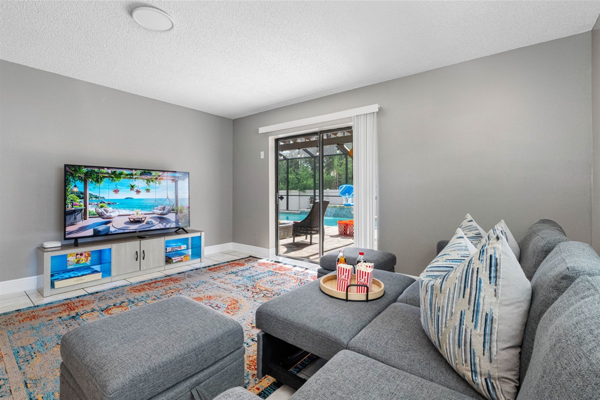 The centerpiece of the room is a modern gray sectional couch, plush and roomy, complete with a pair of matching ottomans for extra legroom or casual seating.