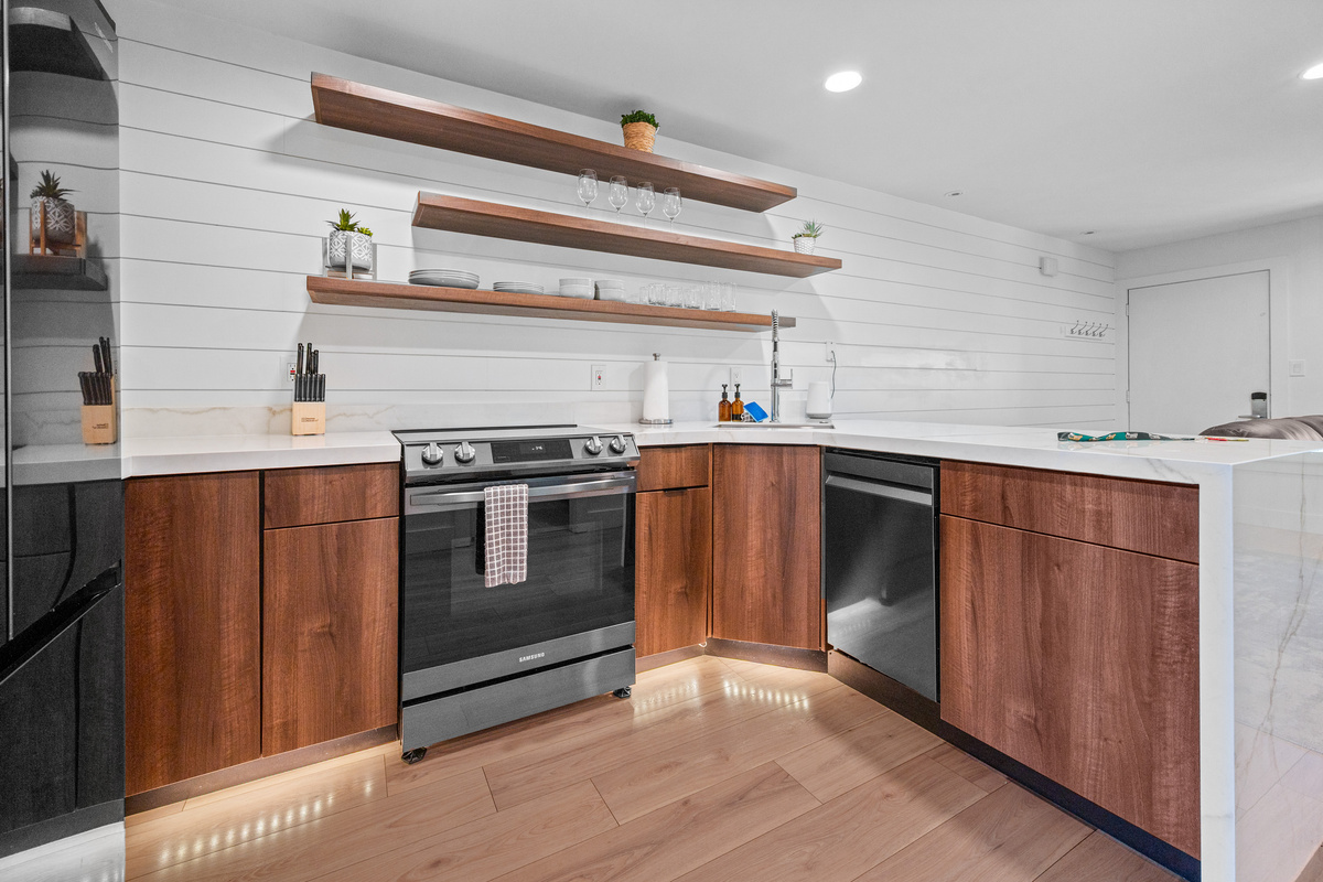 Stylish kitchen with stainless steel appliances, quartz countertops, and open shelving.