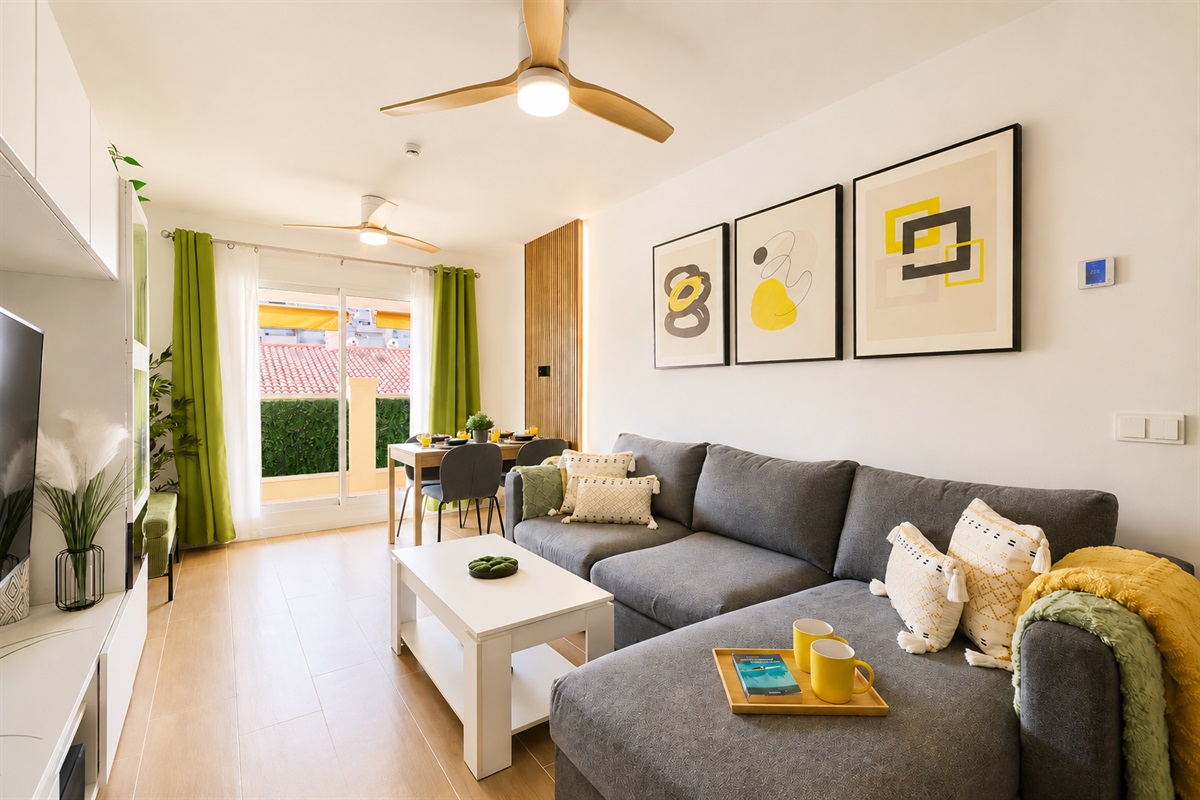 Stylish open-plan living room with a modern kitchen, smart TV, and natural light throughout — ideal for relaxing or sharing a glass of wine after a day by the beach.