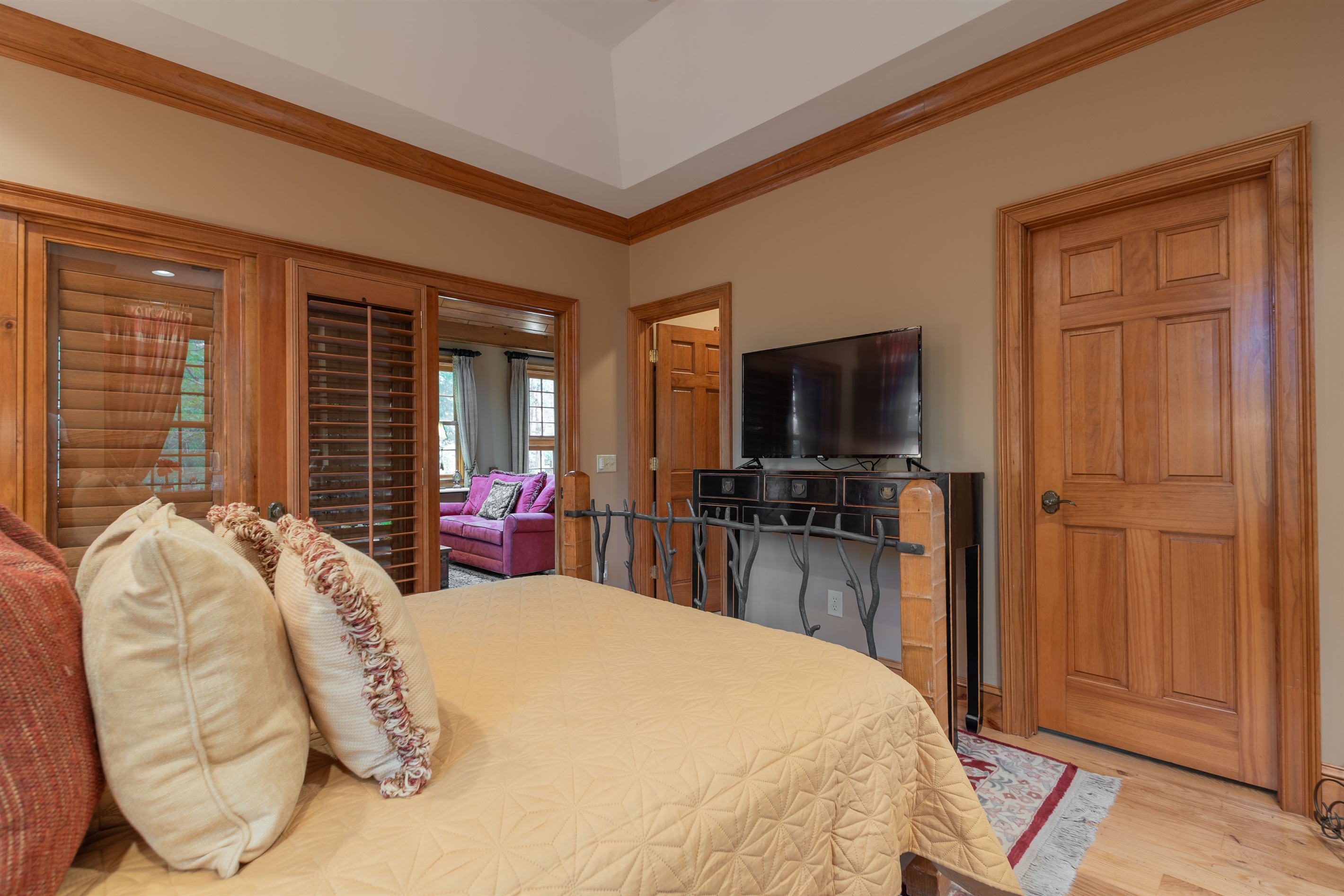The main-level queen bedroom offers a cozy and inviting retreat with warm wood accents, a smart TV, and easy access to the shared en suite bathroom.