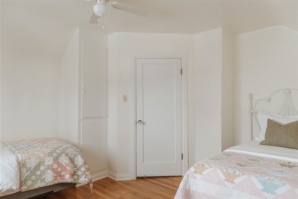 Two twin beds with matching white iron headboards are layered in crisp white linens and pastel quilts.