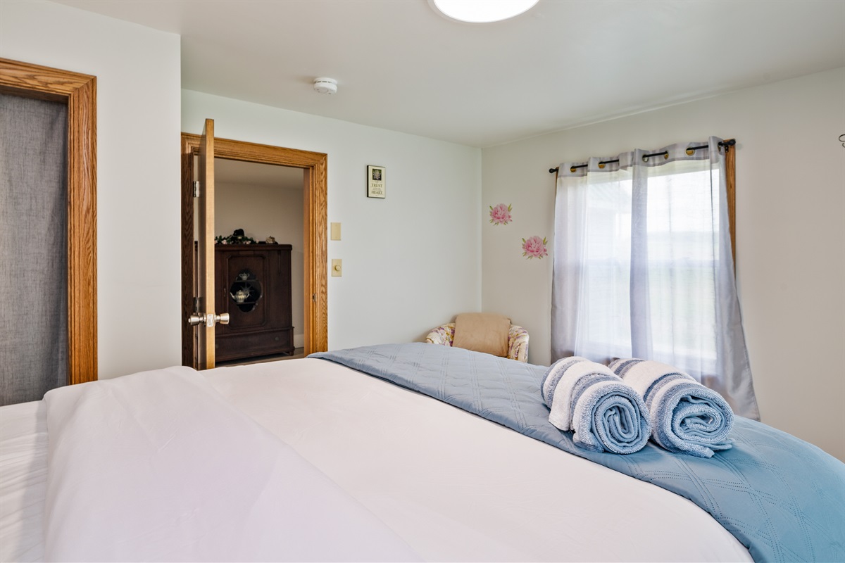 Spacious bedroom with a comfy queen bed, floral accents, and warm natural light—perfect for a restful retreat.