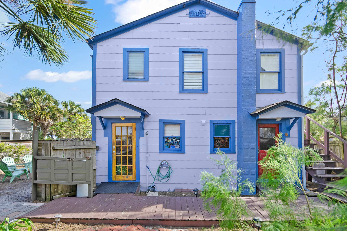 The full front of the building, with your own staircase climbing to the upstairs door. Two separate homes in one historic bungalow, each with its own entrance, its own colour scheme and its own distinct character.
