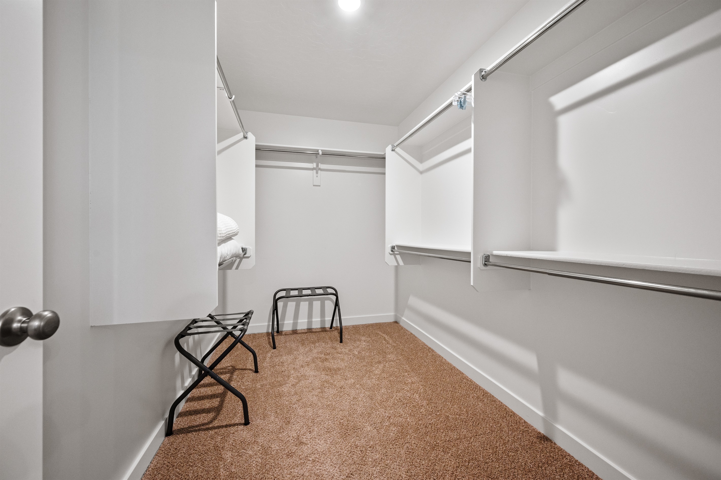 This well-lit walk-in closet includes luggage racks and plenty of space to store clothes, shoes, and travel essentials.