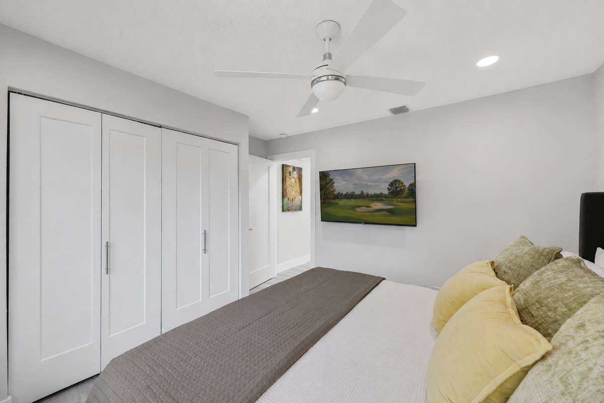A clean king bedroom with a wall-mounted TV, ceiling fan, and closet space gives guests a simple, comfortable place to unwind.