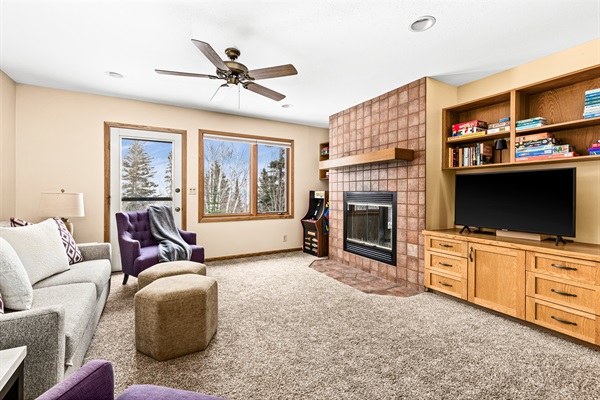 Fun basement living room featuring a mini Pac-Man arcade, a TV for entertainment, shelves stocked with games and books, and comfortable seating. A perfect space for family fun and relaxation.