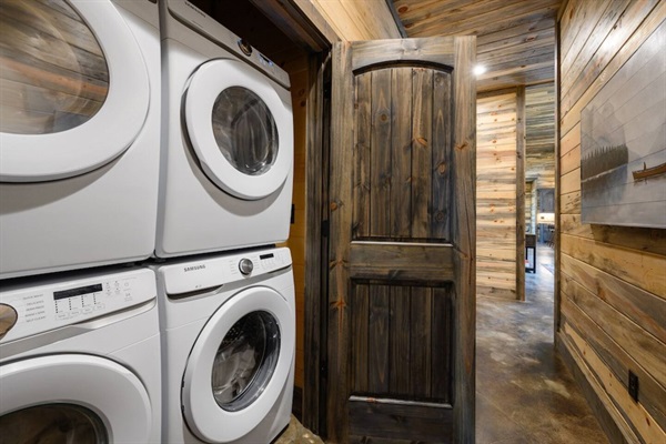 A fully equipped cabin laundry room featuring a stacked washer and dryer, surrounded by beautiful reclaimed wood walls, blending functionality with rustic charm.