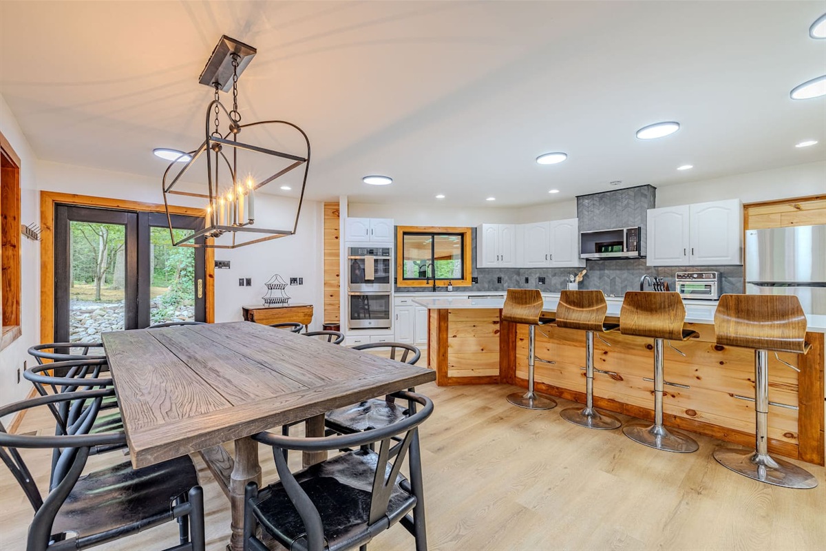 A bright, open-concept kitchen and dining space featuring seating for twelve between the table and island, with effortless access to the outdoor grill for seamless indoor-outdoor entertaining.
