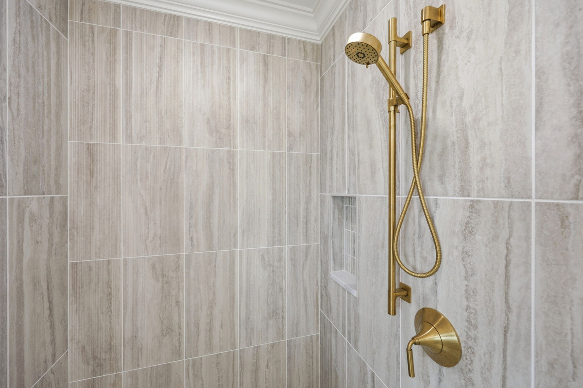 Walk-in shower with vertical stone tile and gold fixtures (master bathroom detail)
