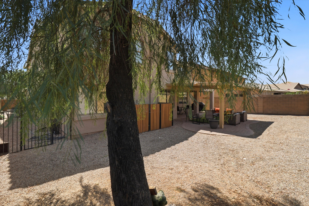 Backyard with a shaded patio, outdoor seating, and a large gravel yard under the trees.
