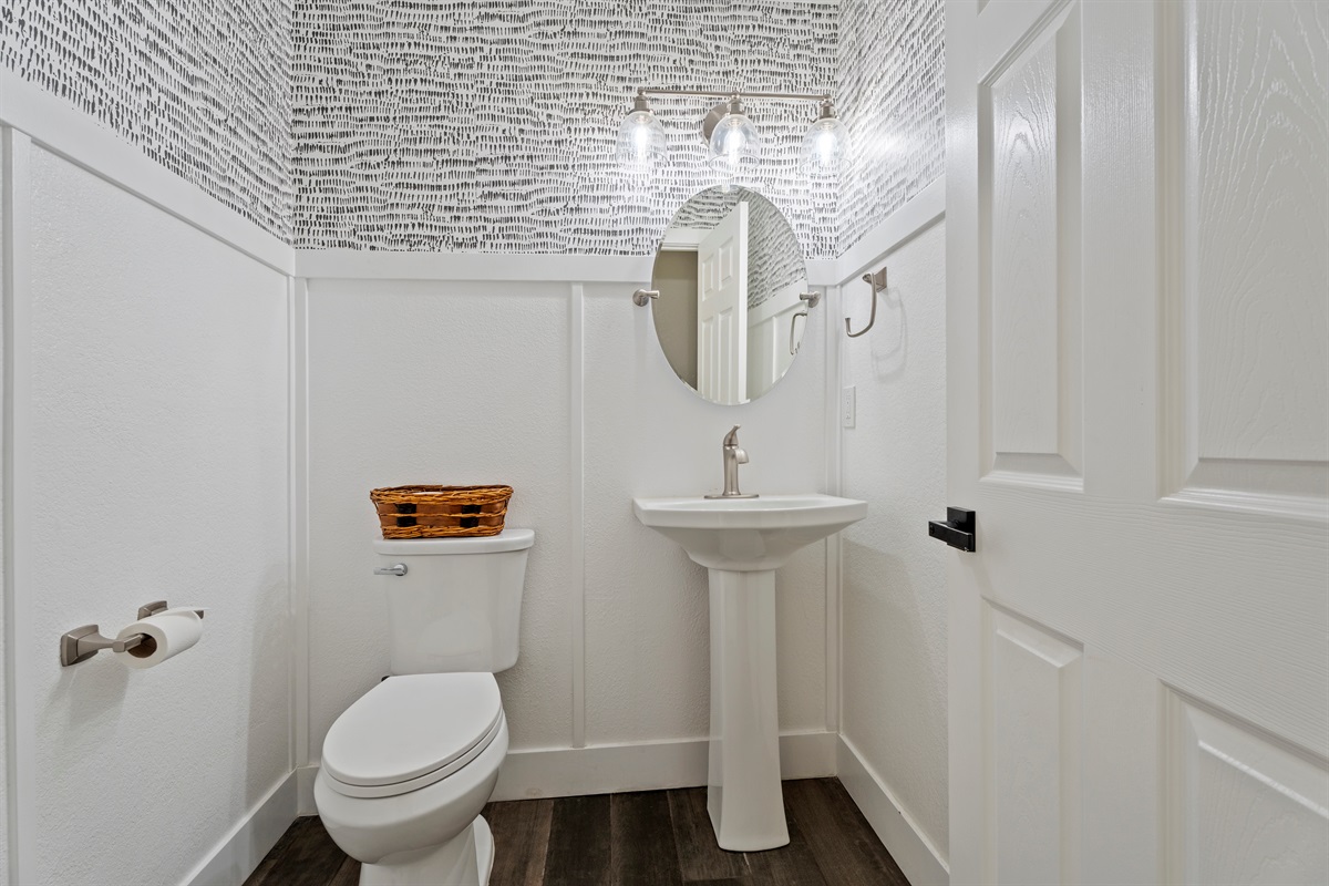 Modern and artistic, this half bath features sleek fixtures, eye-catching wallpaper, and a clean, polished design.
