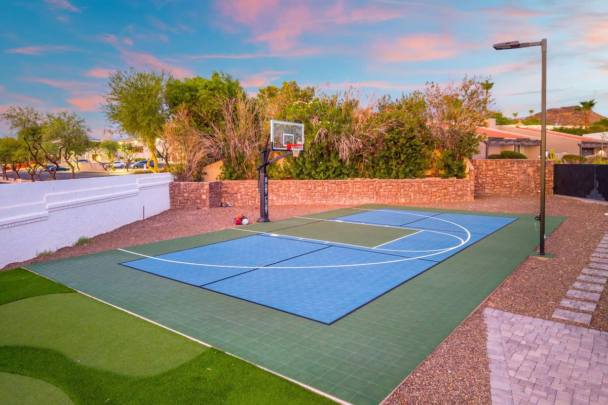 A vibrant blue-and-green sport court glows under a pastel sunset, framed by lush desert landscaping.