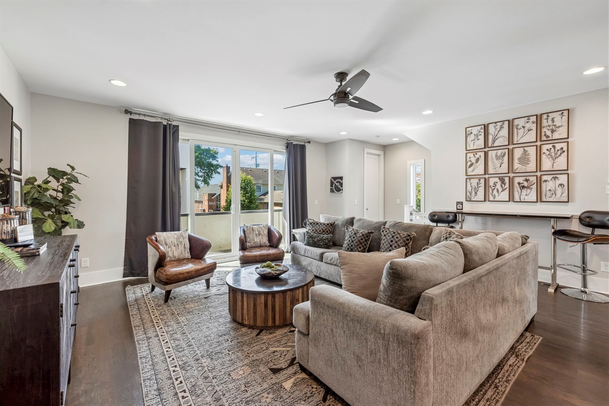 Spacious sectional and accent chairs provide room for the whole group to relax - Natural light pours through large windows, highlighting the clean, modern design - Botanical wall art and bar seating blend comfort with visual interest and function