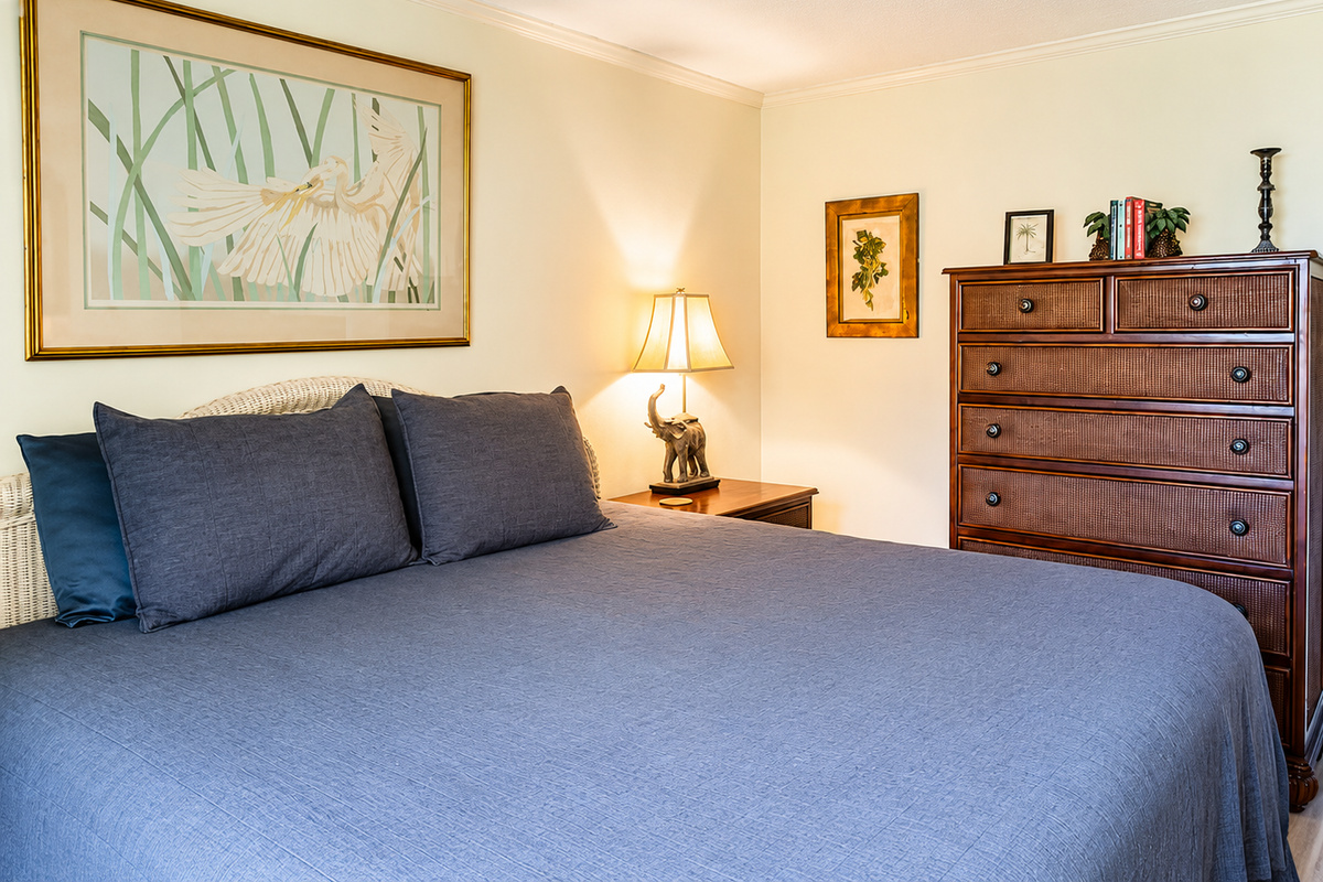Cozy bedroom with blue‑gray bedding, wooden dresser, and warm decorative accents.