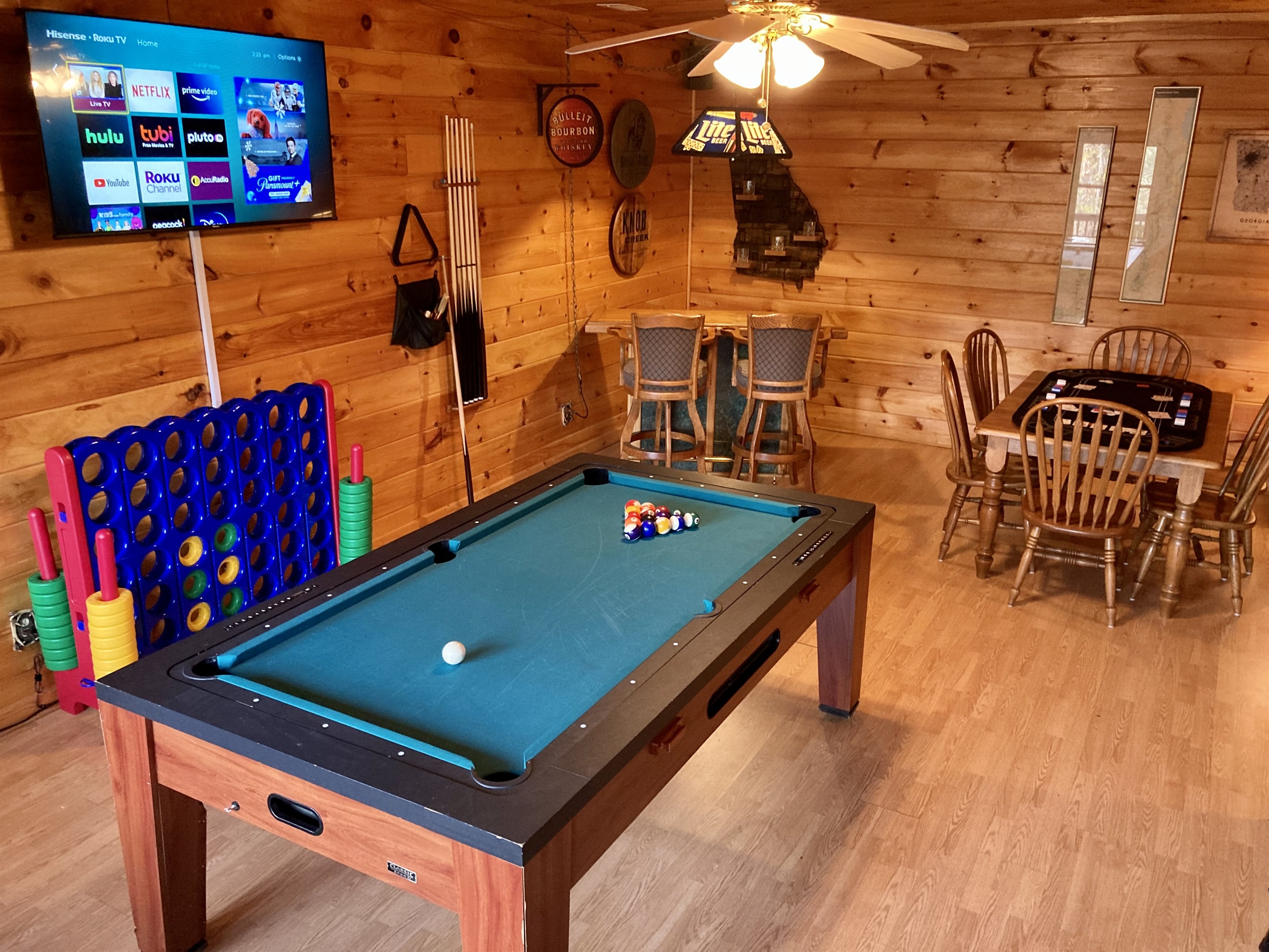 Game room with giant Connect Four, pool table (converts to ping pong), Roku Smart TV, whisky-themed bar area, and table with six chairs.