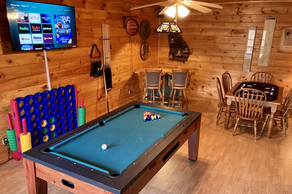 Game room with giant Connect Four, pool table (converts to ping pong), Roku Smart TV, whisky-themed bar area, and table with six chairs.