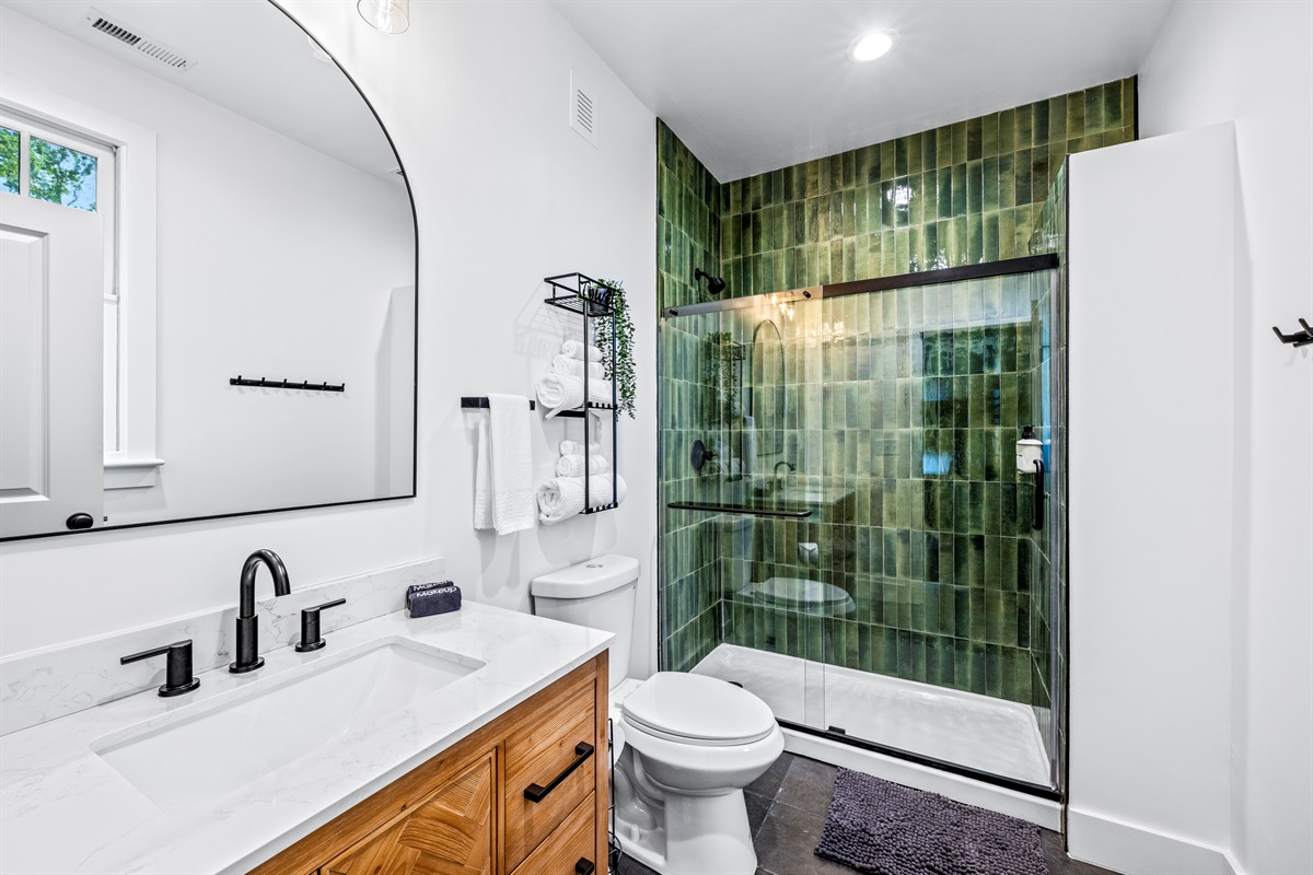 This spa-inspired ensuite features a striking green tiled shower, modern fixtures, and thoughtful touches to elevate your stay.