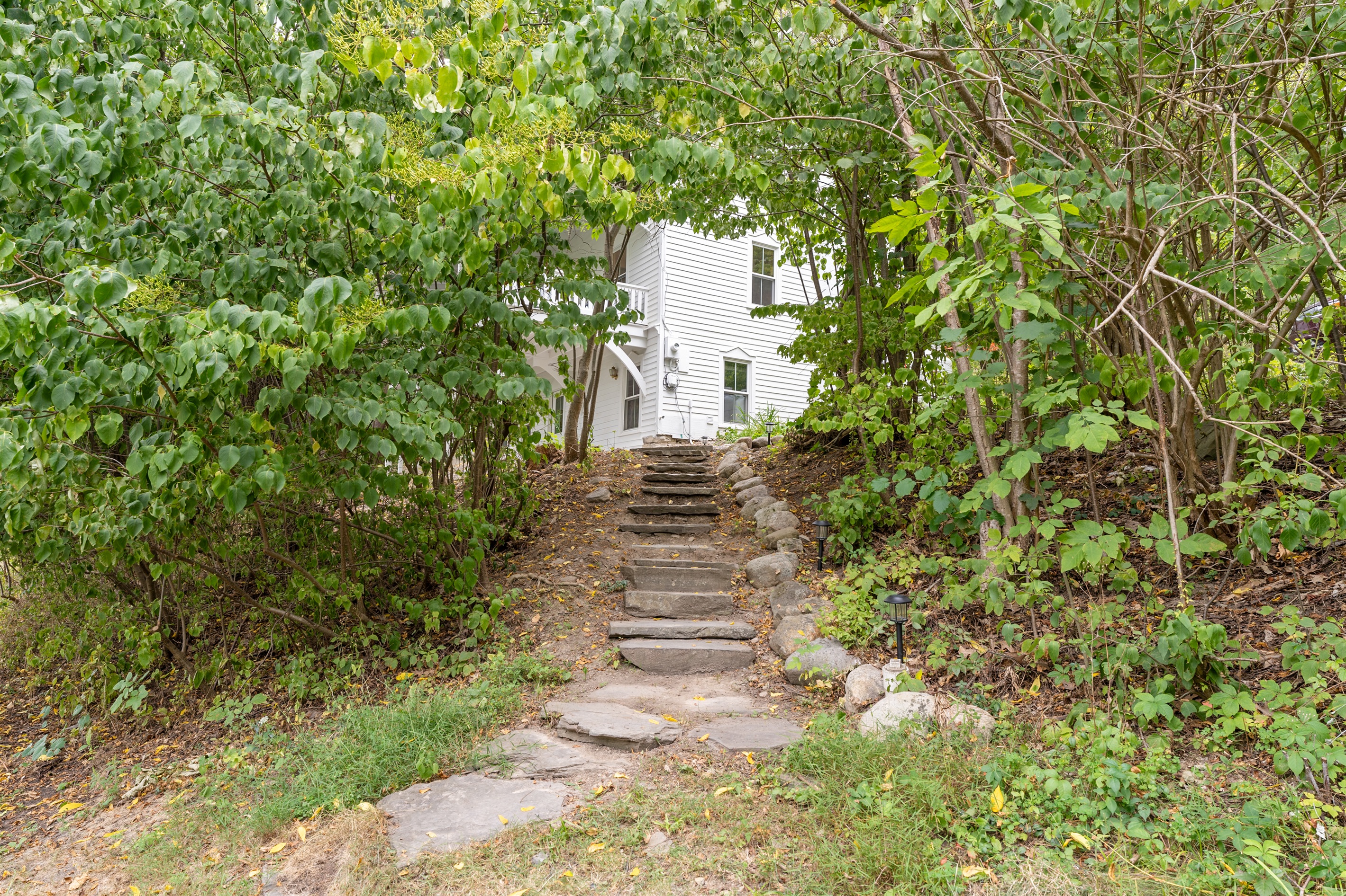 Rustic stone pathway leads through the trees to this inviting lakeside retreat, blending history with nature.