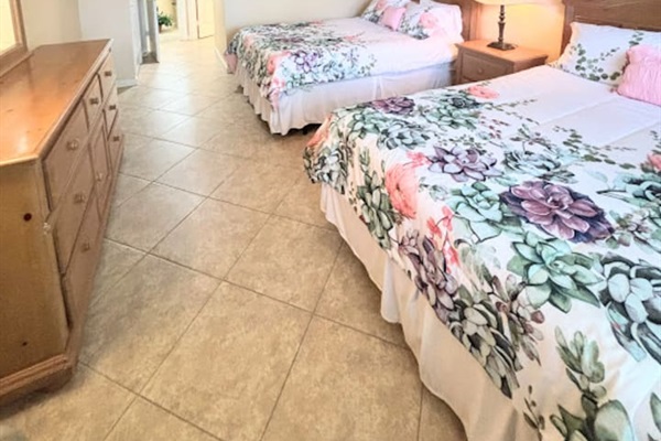 Comfortable bedroom featuring two beds, tile flooring, dresser storage, and a bright, welcoming setup.