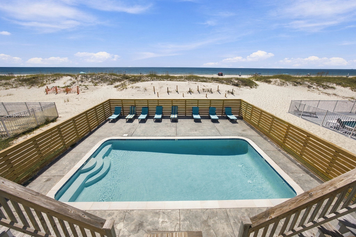 Swimming pool surrounded by a spacious deck and outdoor lounge chairs at the beach vacation property.