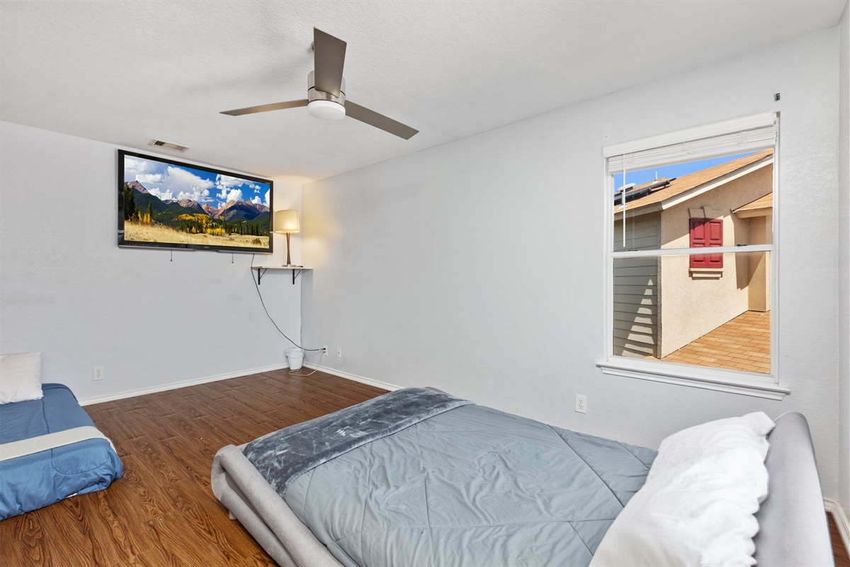 Queen and twin bedroom with wall-mounted Smart TV and streaming. Ceiling fan, room-darkening shades, and hotel-quality bedding. Current decorative blankets, bedding, and wall art are not shown in these photos.