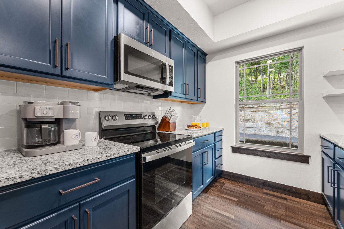 The fully equipped navy kitchen has granite counters, stainless appliances, a coffee bar, and a creekside window.