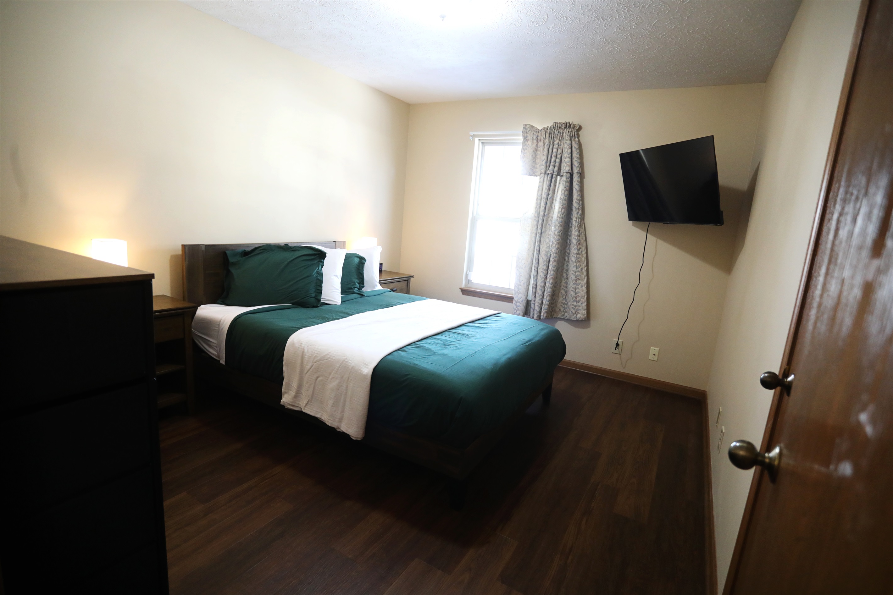 NE bedroom showing showing queen size bed, Roku TV, dresser, nightstands with touch lamps, and alarm clock