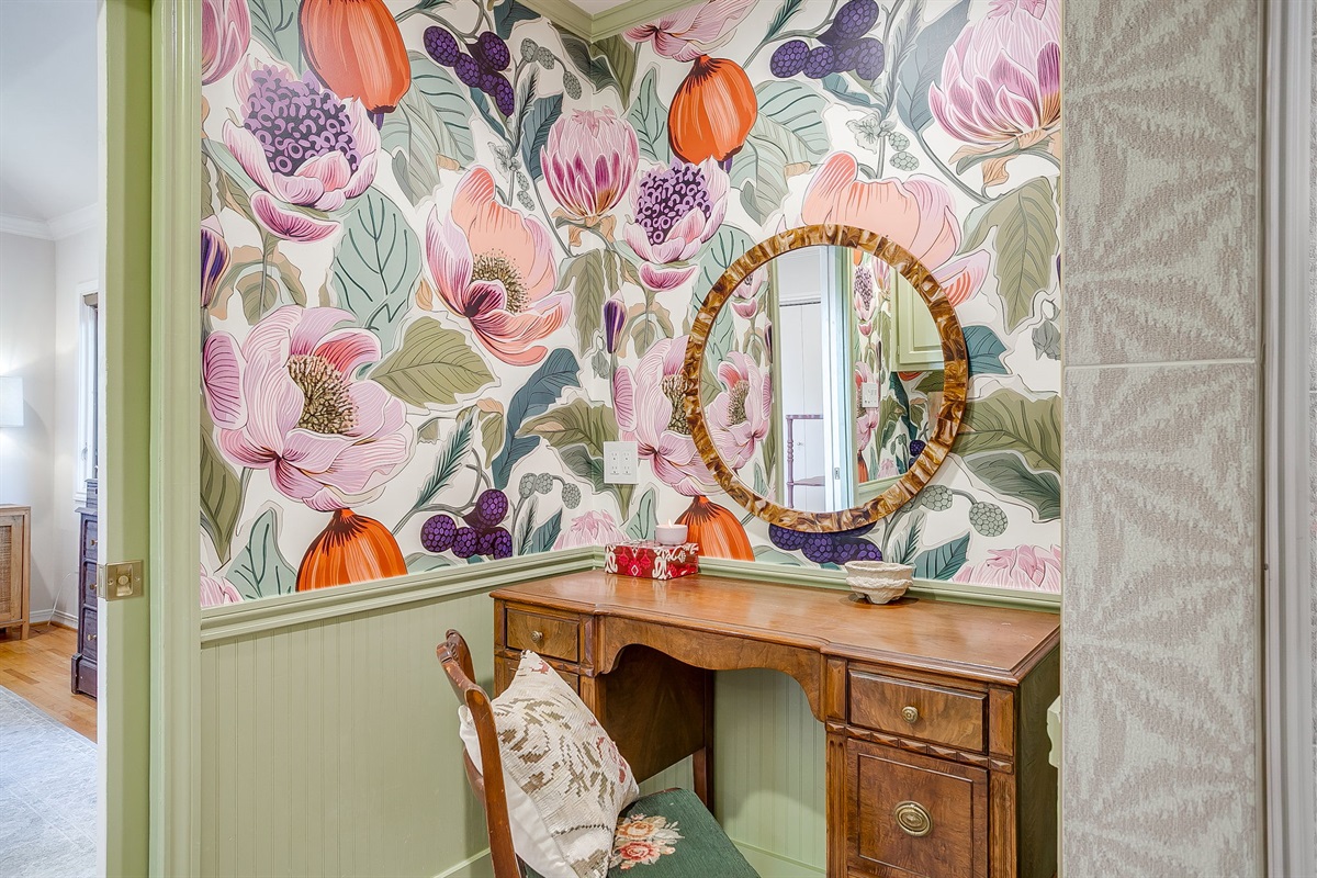 Rear bath with a bonus glam nook — a dedicated makeup vanity separate from the sinks, wrapped in bold floral wallpaper and bright, happy color.