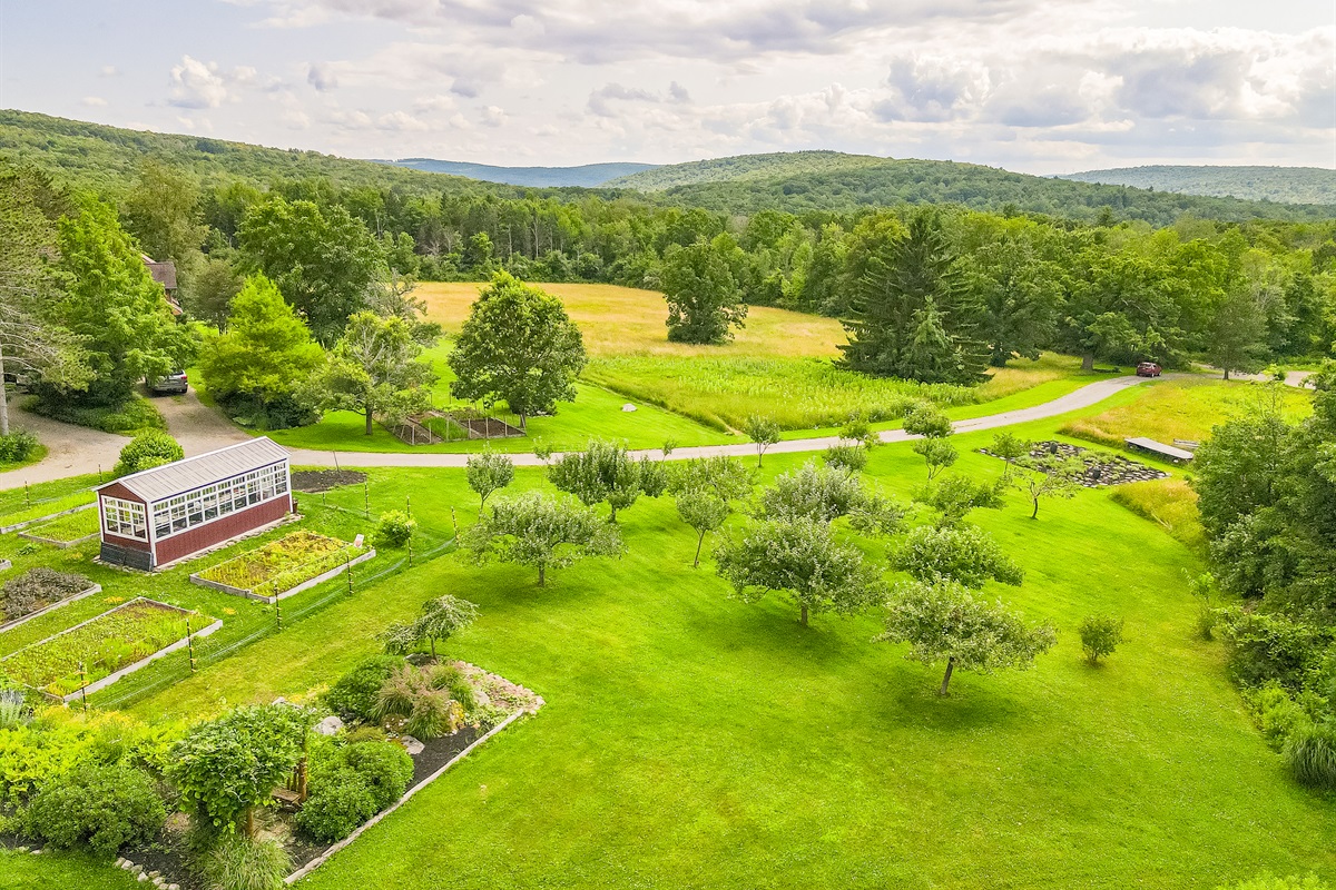 Charming country living with a classic red barn, greenhouse, and lush garden beds surrounded by nature’s beauty.