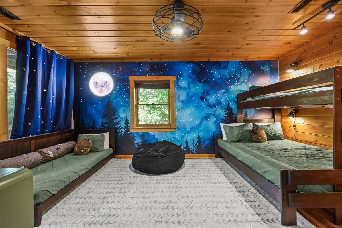 Full view of the bunk room with a twin XL over a queen that have a sconce beside each bed as well as a twin daybed. This room has a tv as well.