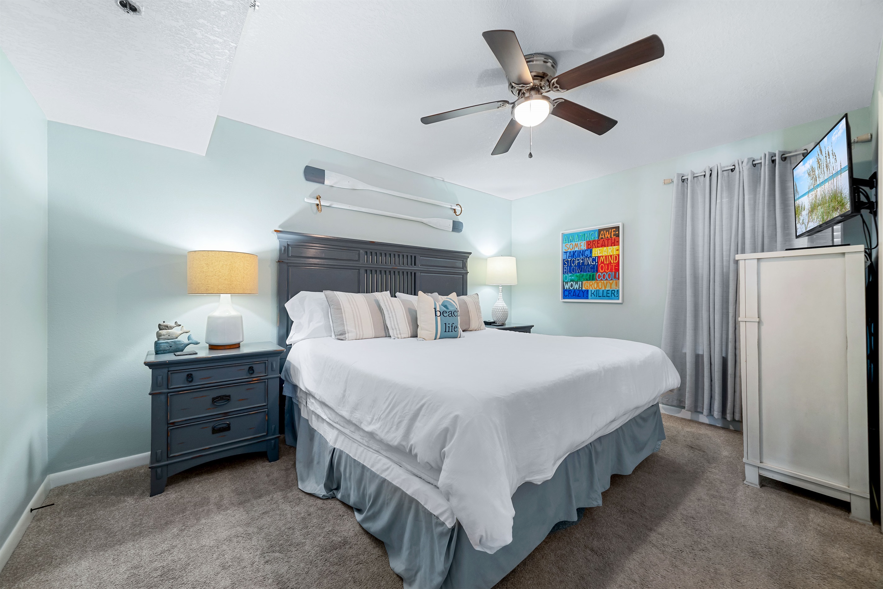 Unwind in the spacious Primary Bedroom, featuring a comfortable King-sized bed and soothing, coastal-themed decor. The room provides a peaceful sanctuary complete with a flat-screen TV and ample storage for a relaxing stay.