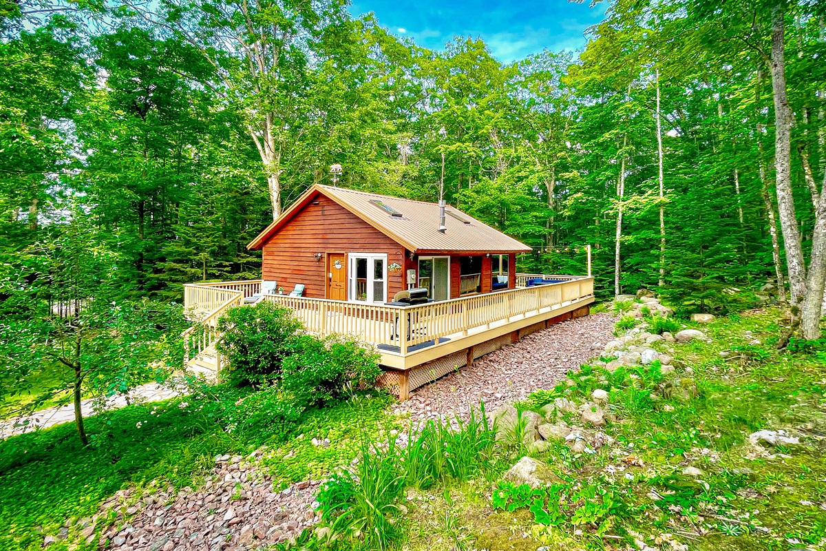 Summer view of the Main Cottage. Apple tree out front & front lounge chairs, 1k wrap around deck. Back deck dining table & lounge couch, propane fireplace (seasonal outdoor furniture May-Oct)