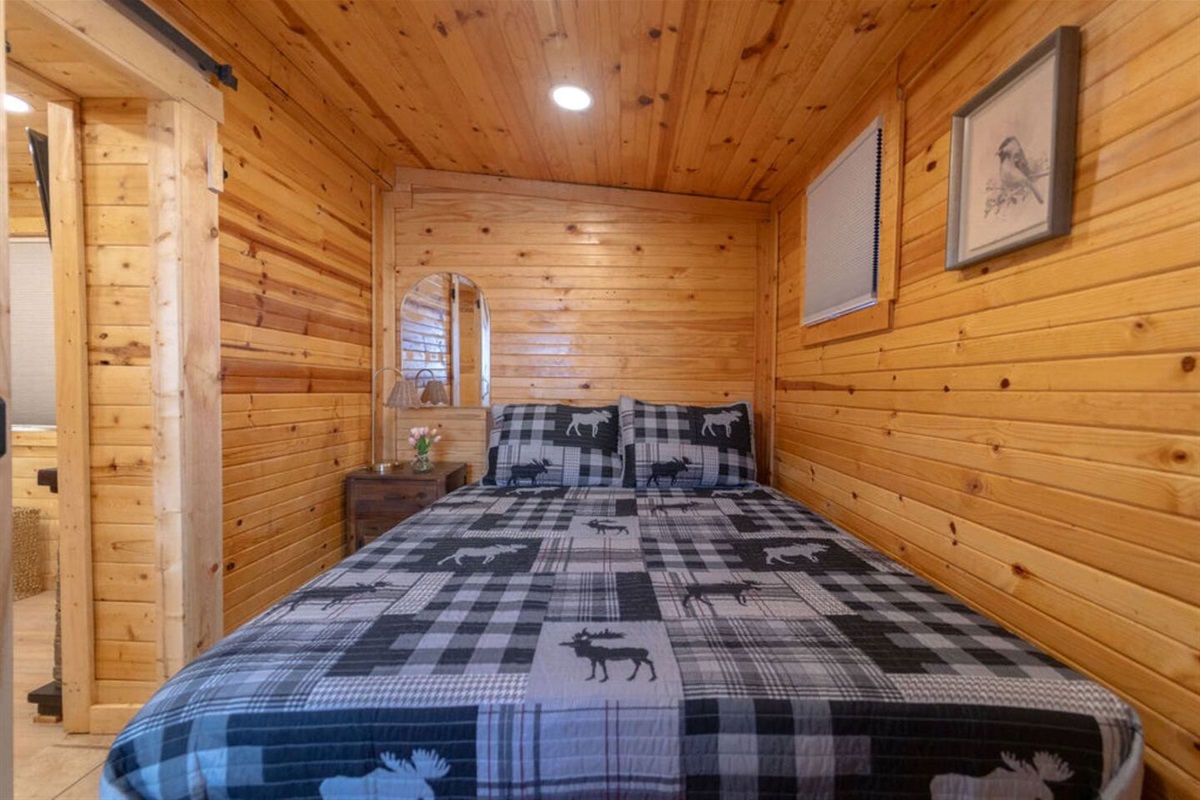 Wake up to the charm of cozy cabin living, with the rustic barn door open to the inviting living room. This comfortable queen bed, surrounded by warm T&G paneling, offers the perfect blend of privacy and connection.
