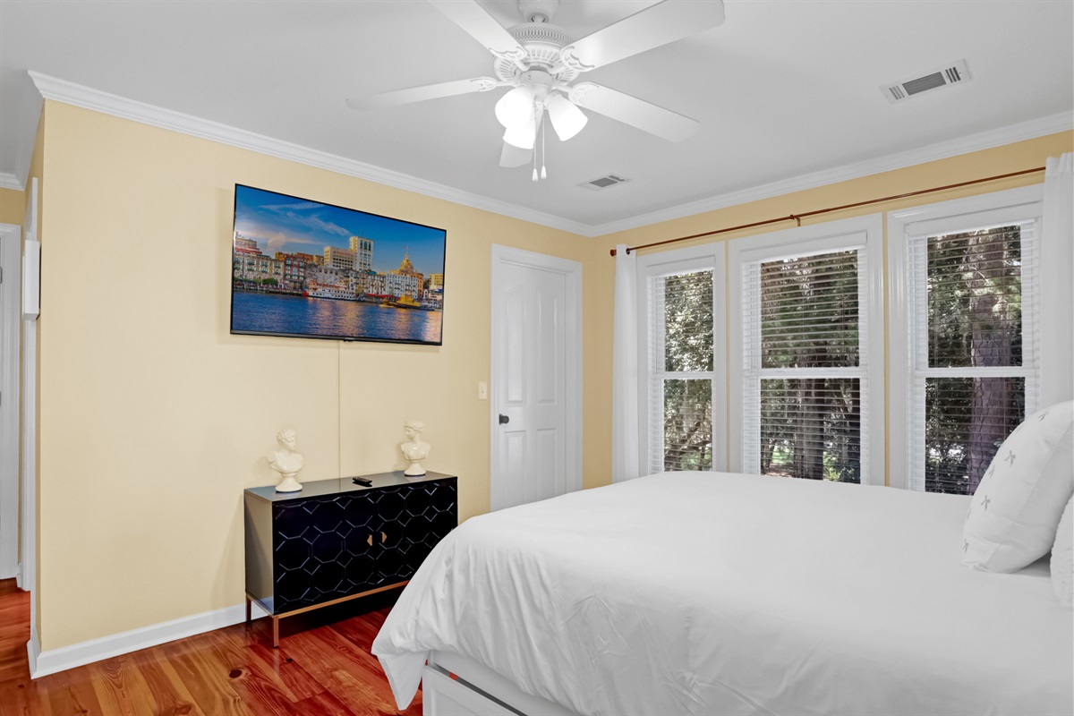 Serene bedroom with a plush bed, natural light from large windows, and a flat-screen TV for relaxing in comfort.