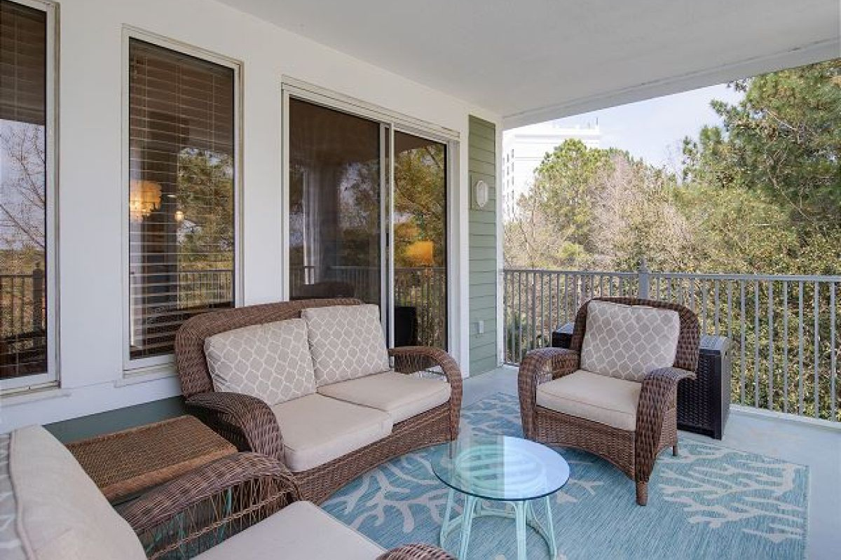 Covered balcony with wicker loveseat and armchairs, outdoor rug and glass side table