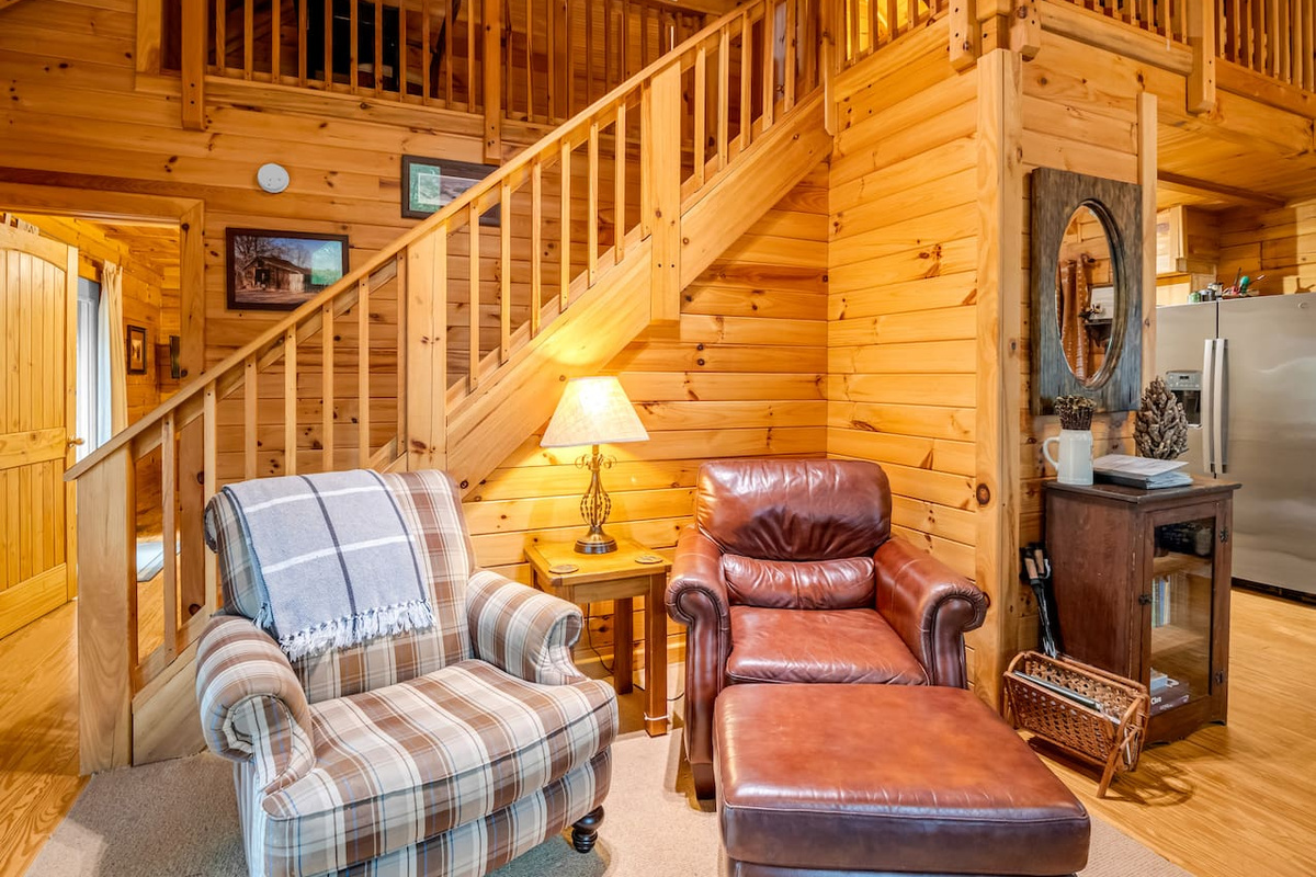 Cozy living room seating area with comfortable chairs, warm cabin charm, and staircase access to the loft