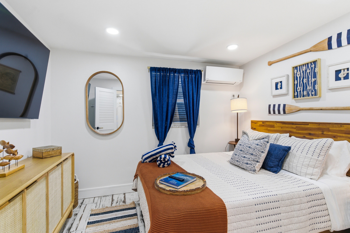 Bedroom 2 has everything you need to recharge — a plush queen bed, wall-mounted TV, cane dresser, dedicated mini split, and nautical décor details that carry the Sail house theme throughout.