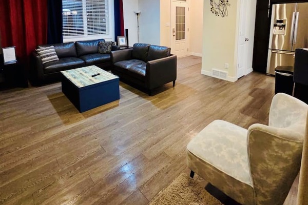 Stylish open-plan living with leather sofas, hardwood floors, and stainless fridge.