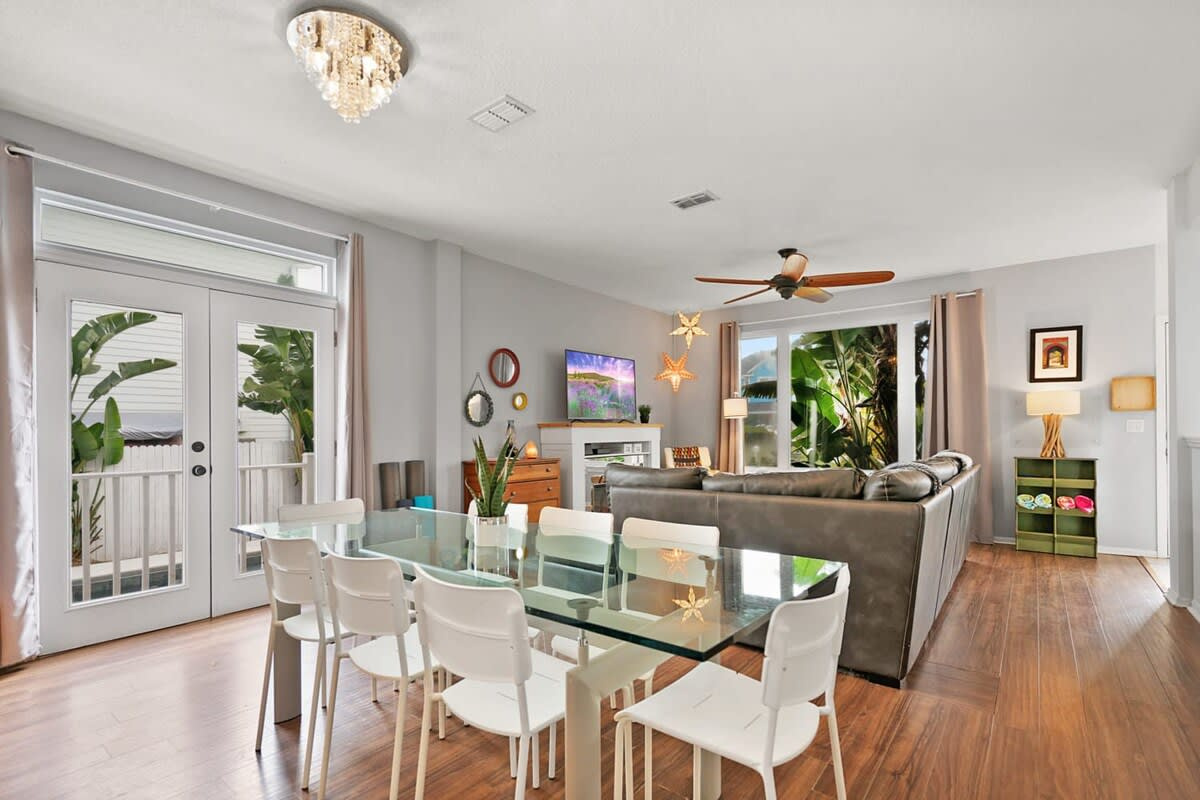 The dining table sits between the kitchen and the living room, so nobody is ever shut away on their own. Ceiling fan overhead, the pool just outside, and room enough round the table for all ten of you.