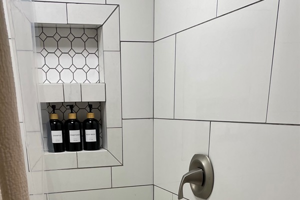 Walk-in tile shower with built-in niche and provided shampoo, conditioner, and body wash