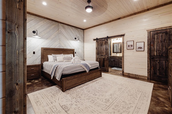 Beautiful rustic bedroom with a king-size bed, wood-paneled walls, barn doors, and warm lighting. The perfect mix of modern farmhouse and luxury cabin retreat.